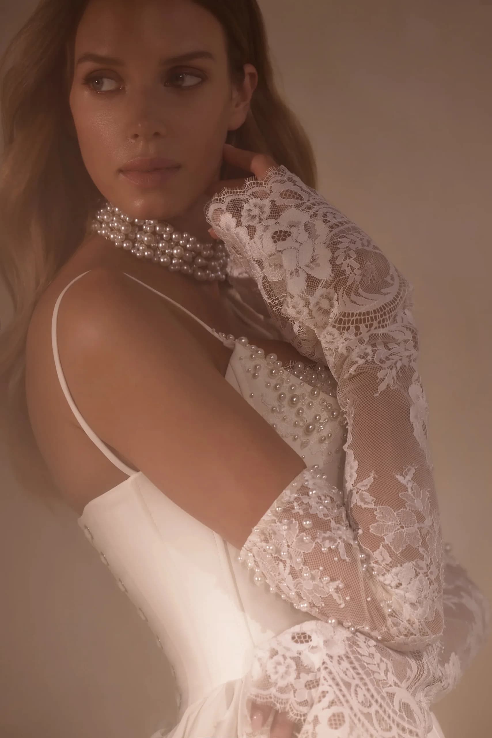 Back view of a bride in a lace and beaded gown with a low open back and long sheer lace sleeves