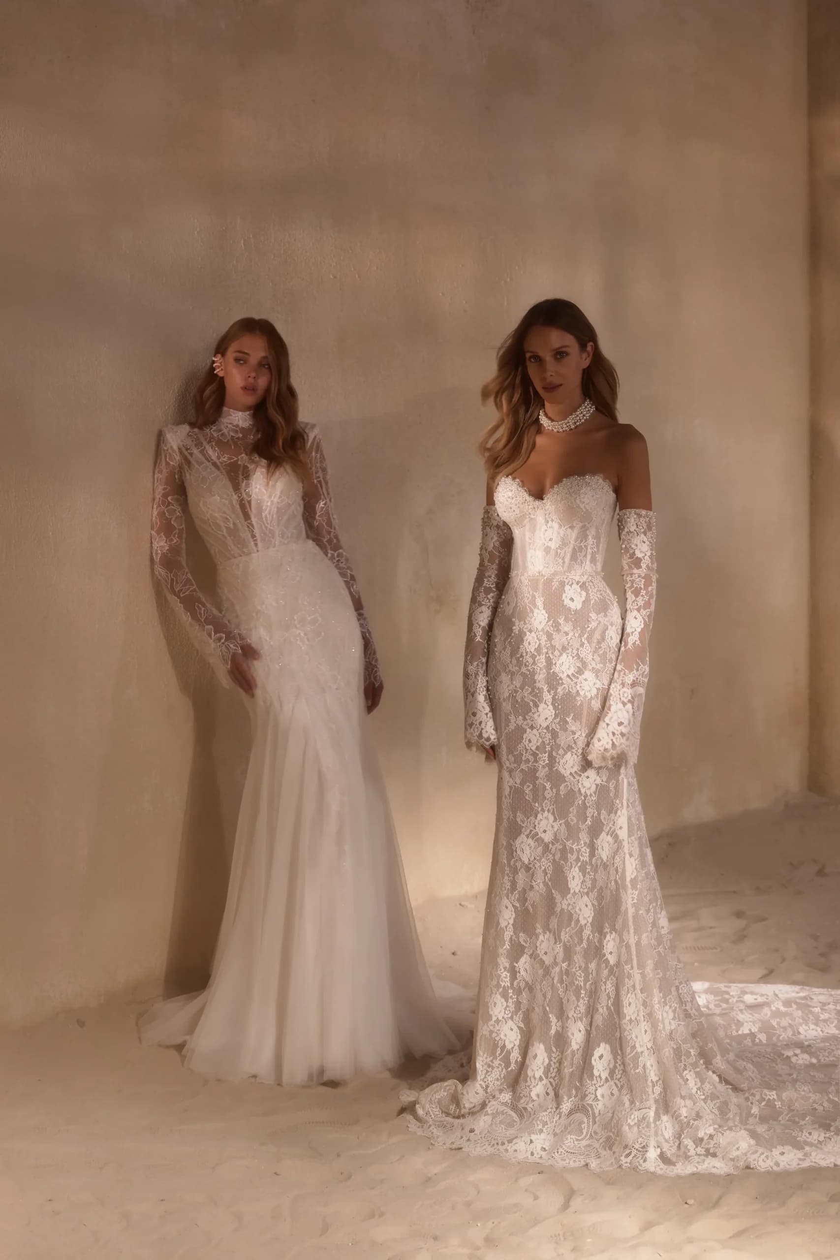 Two brides wearing lace gowns with long sleeves, one in ivory with a high neckline and the other in cream with an off-shoulder sweetheart neckline