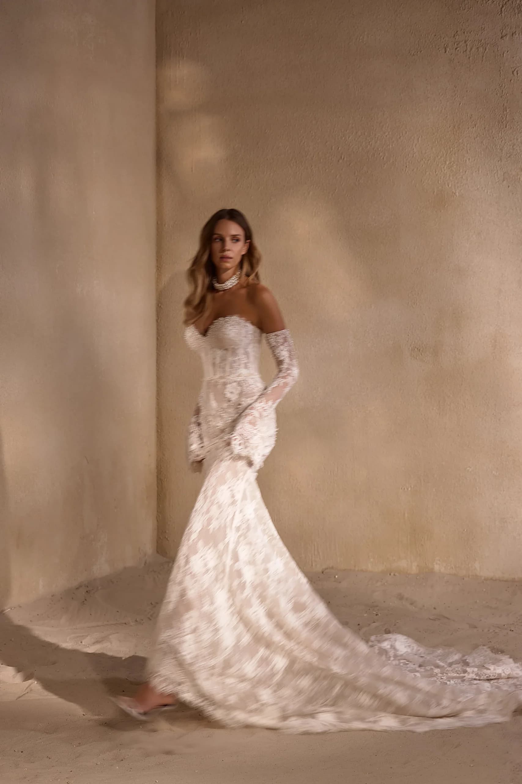 Bride in profile wearing a mermaid gown with fitted lace bodice and long sleeves, skirt flaring dramatically at the knee with a sweeping train